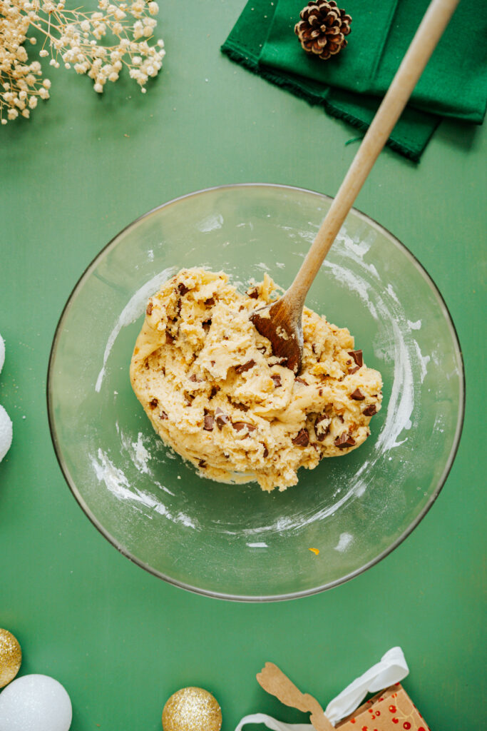 Boules de pâte à cookie. Ingrédients pour la préparation de cookies : farine, sucre, beurre fondu, œuf, chocolat, levure et vanille, joliment disposés sur un fond vert avec des décorations festives. Astuces pour réussir et sublimer ses cookies