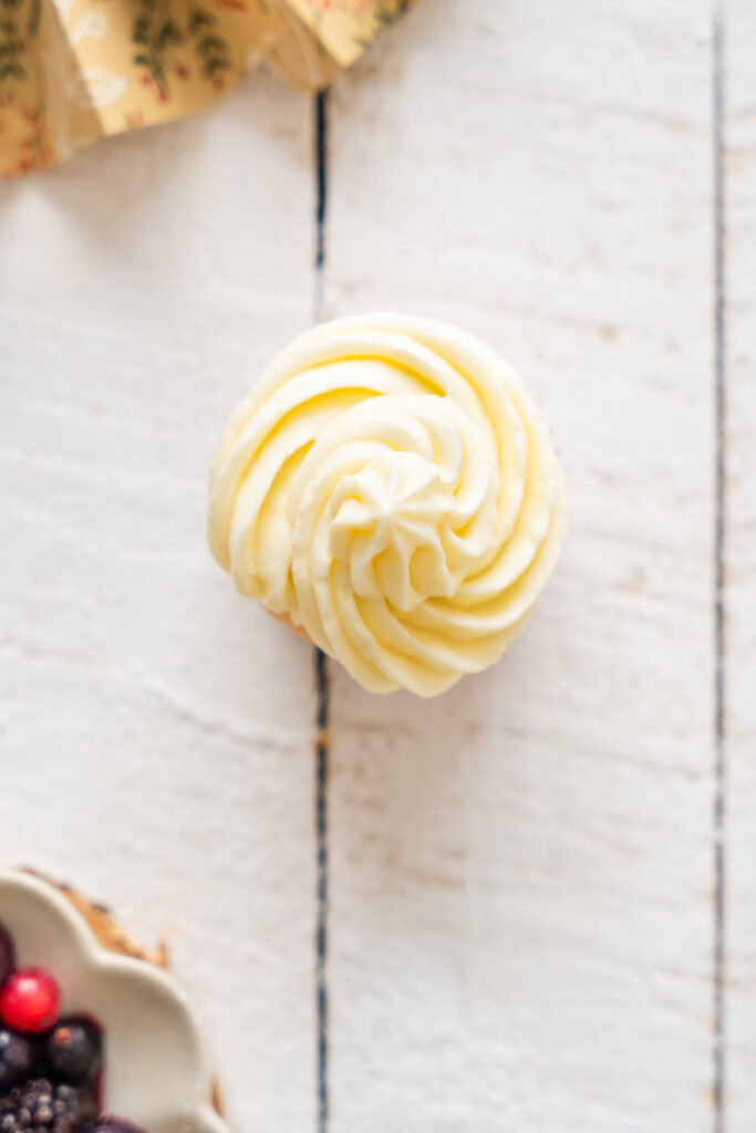 Cupcake vue du dessus avec un topping à la crème, posée sur une planche en bois.