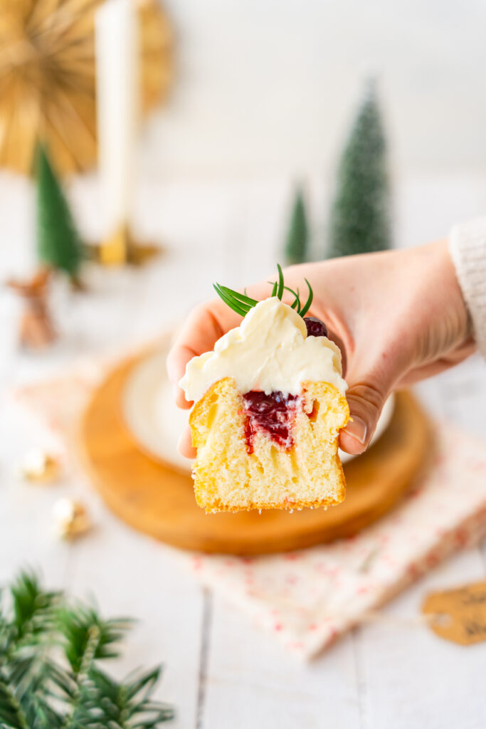 Cupcake coupé en deux, avec un cœur de confiture de fruits rouges, un topping à la crème et des baies en décoration, sur une assiette en céramique posée sur une planche en bois.