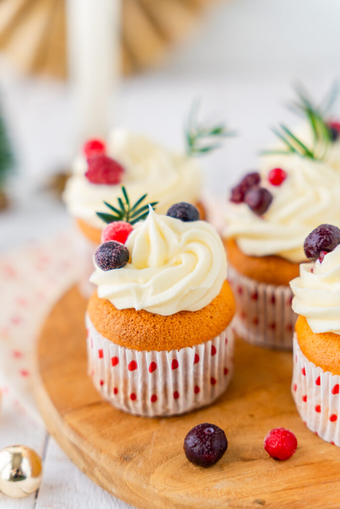 Cupcakes coupés en deux, avec un cœur de confiture de fruits rouges, un topping à la crème et des baies en décoration, sur une assiette en céramique posée sur une planche en bois.
