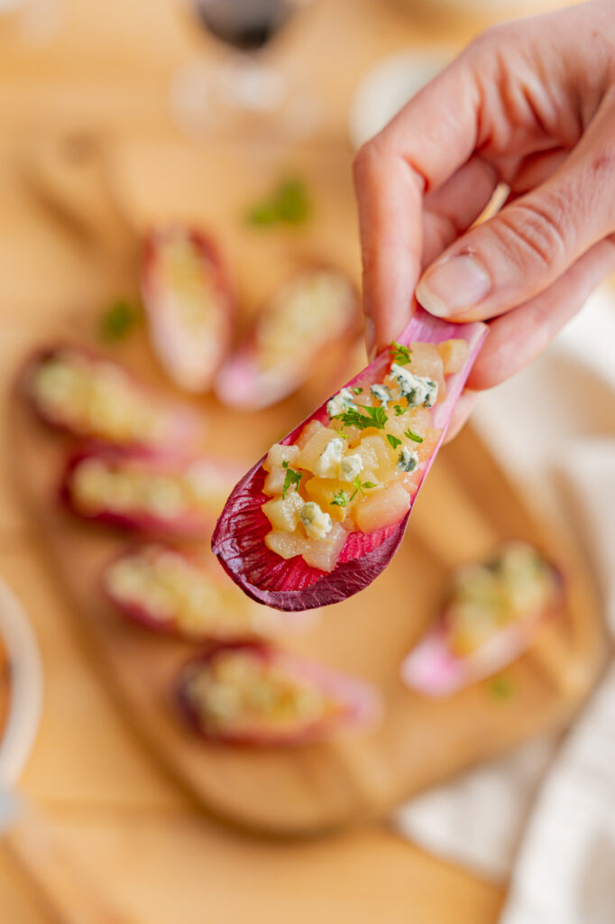 Amuse-bouches endives, poire bleu et miel. Recette à base de feuilles de chicorée garnies de fromage et de noix, disposés sur une planche en bois avec du pain et du miel.